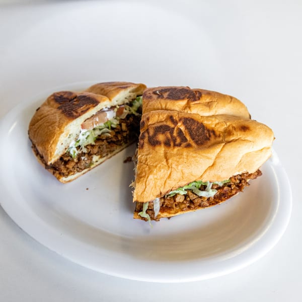 A Mexican torta sandwich, cut in half, filled with meat, lettuce, and crema on a white plate.