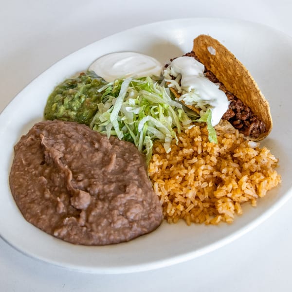 A hard-shell taco with ground beef, lettuce, and sour cream, served with rice, refried beans, and guacamole.