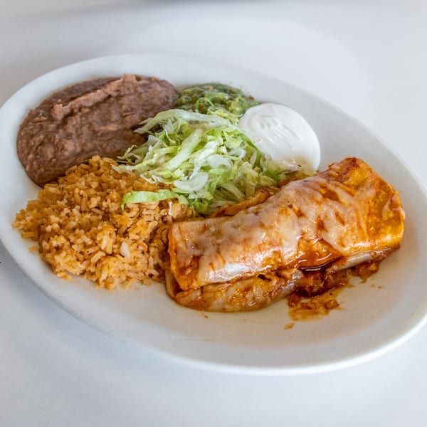 A Mexican combination plate with an enchilada, rice, refried beans, guacamole, shredded lettuce, and sour cream.