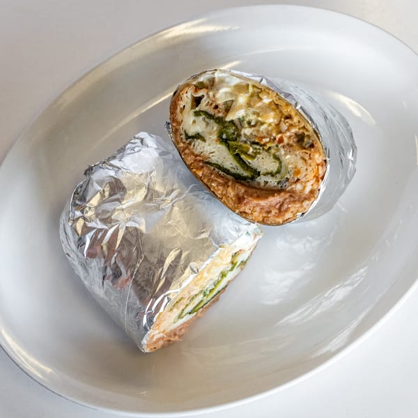 A Mexican burrito, cut in half and wrapped in foil, sits on a white plate.