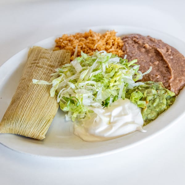 Mexican tamale plate with rice, refried beans, shredded lettuce, guacamole, and sour cream.