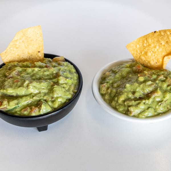 Two bowls of chunky guacamole with tortilla chips, one in a black bowl, one in a white bowl.