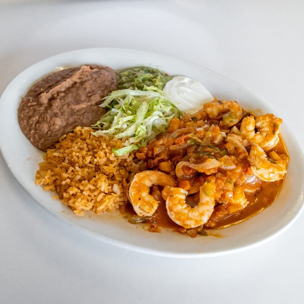 Shrimp dish with rice, refried beans, guacamole, sour cream, and shredded lettuce on a white plate.