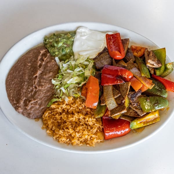 A Mexican dish with steak fajitas, rice, refried beans, guacamole, sour cream, and shredded lettuce.